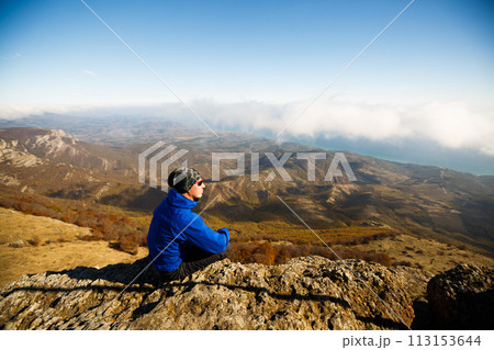 Man meditating on a mountain peak rock. Hiker enjoy the scenery above clouds on summit 113153644