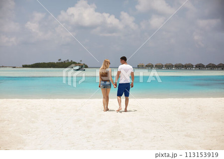 Back view of couple holding hands and walking to the blue ocean lagoon on Maldives at luxury spa resort. Travel and honeymoon concept. 113153919