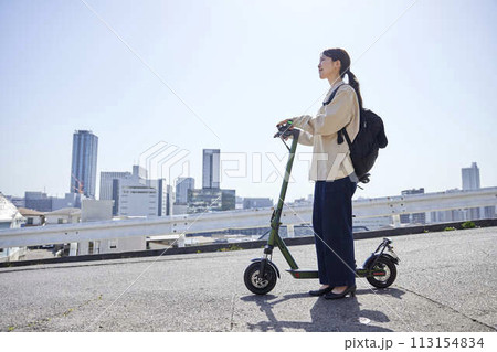 都市の近距離移動をする電動キックボードの女性 113154834