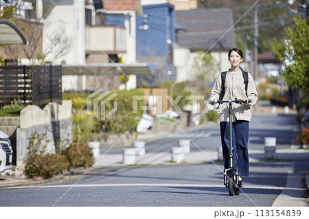 住宅街を電動キックボードで移動する日本人の女性 住宅街を電動キックボードで移動する日本人の女性 113154839