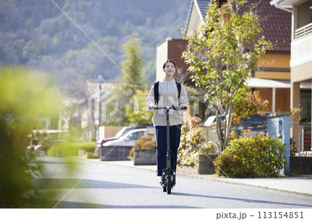 住宅街を電動キックボードで移動する日本人の女性 住宅街を電動キックボードで移動する日本人の女性 113154851