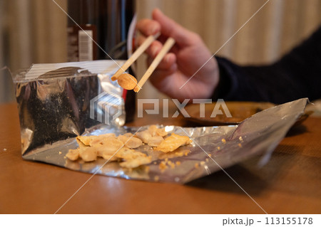 お菓子を箸で摘まんで食べる　手が汚れないように箸を使ってスナックを食べる手元 113155178