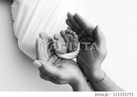 The palms of the father, the mother are holding the foot of the newborn baby. Feet of the newborn on the palms of the parents. Studio macro black and white photo of a child's toes, heels and feet. 113155775