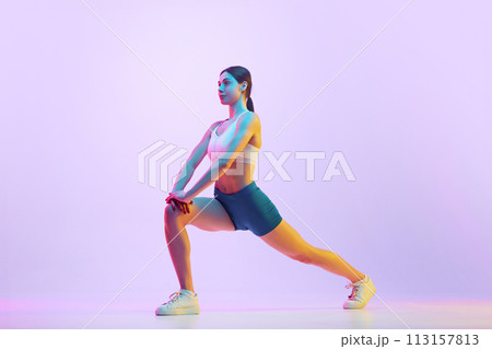 Young athlete woman doing lunges in motion in neon light against gradient studio background. Side view portrait. Young athlete woman doing lunges in motion in neon light against gradient studio background. Side view portrait. 113157813
