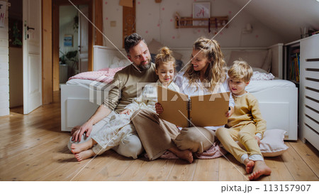 Beautiful family sitting in kids room on floor, looking at old family photos in photoalbum. Calm hygge family moment. 113157907