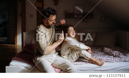 Father combing and braiding daughter's hair as part of bedtime routine. Single dad taking care of his daughter's hairstyle. 113157911