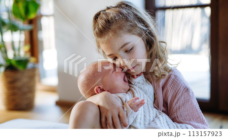 Portrait of big sister soothing newborn sister. Girl taking care of crying baby. Sisterly love, joy for new family member. 113157923