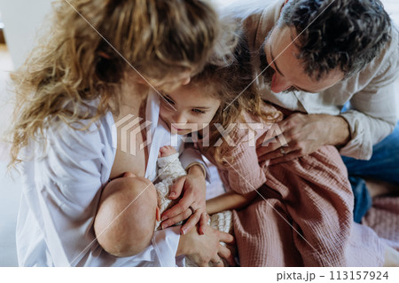 Mother breastfeeding newborn, big sister looking at new baby in mom's arms. Strong family, bonding and parents' unconditional love for their children. 113157924