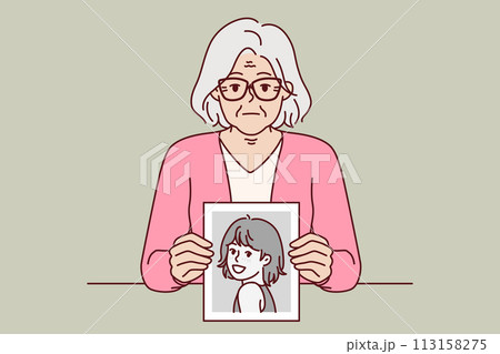 Elderly woman remembers youth, showing portrait from past, and looks at screen with slight sadness 113158275