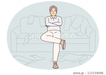 Bachelor man sits on couch among scattered clothes and is too lazy to start cleaning 113159046
