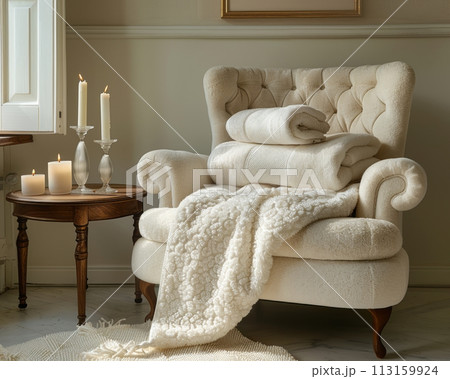 A stack of towels and an armchair with candles, a wall in the background, 113159924