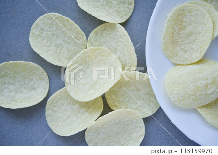 Potato chips on a gray background. Pour the chips into a saucer. A delicious snack. Potato chips on a gray background. Pour the chips into a saucer. A delicious snack. 113159970
