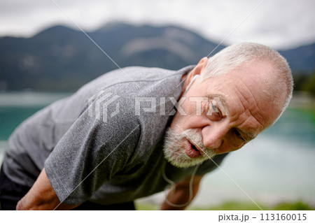 Senior breathing after run by lake in nature. Elderly man exercising to stay healthy, vital, enjoying physical activity and relaxation outdoors. Senior breathing after run by lake in nature. Elderly man exercising to stay healthy, vital, enjoying physical activity and relaxation outdoors. 113160015