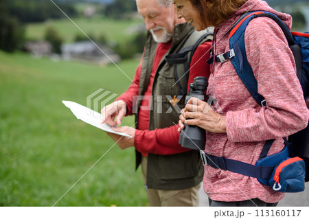 Active elderly couple hiking together in mountains, enjoying nature. Senior tourists looking at route on map. 113160117