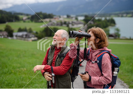 Active elderly couple hiking together in autumn mountains. Senior tourists enjoying nature look through binoculars. Active elderly couple hiking together in autumn mountains. Senior tourists enjoying nature look through binoculars. 113160121