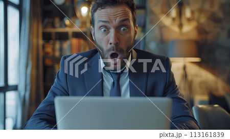 A businessman in a suit sits at a laptop with an open mouth gesture 113161839