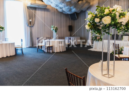 Decorated interior for festive event. Fancy table set for dinner with flower composition in restaurant, luxury interior background. Wedding elegant banquet decoration arranged by catering service 113162700