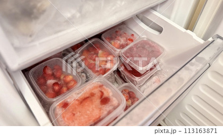 Freezer and frozen strawberries and raspberries in transparent plastic containers. Close-up 113163871