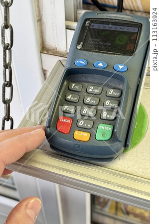 Close-up of a payment terminal lying on a table for paying for goods using plastic cards. The finger of an unknown person enters the PIN code. Close-up 113163924