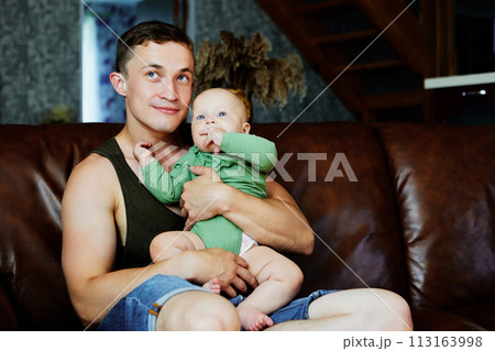 Father with baby daughter in his arms sits on leather sofa at home. 113163998