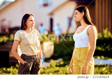 Two young European women are having conversation on rural street on summer day. Two young European women are having conversation on rural street on summer day. 113164024