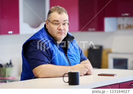 Sad large build man sits in front of kitchen island. 113164027
