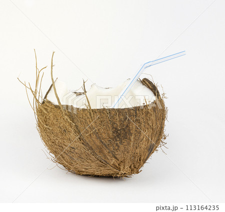 Close-up of half a coconut with a tube in the middle. A glass made of coconut. 113164235