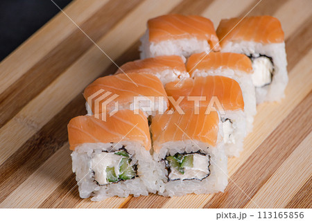 Philadelphia sushi roll on wooden bamboo tray on black background. Popular Asian dish of rice and salmon. Fast delivery of Japanese takeaway food. 113165856