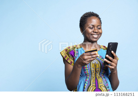 African american girl doing online shopping and paying for clothes with card, entering banking details and numbers to complete money transaction. Female model buying items on internet. 113168251