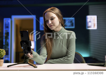 Content creator using smartphone on phone holder as recording gear to shoot intro for vlog channel on online platforms. Internet star warmly welcoming dedicated fanbase, filming with cellphone 113168300