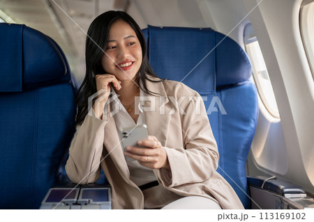 An attractive Asian businesswoman is sitting at the window seat with a smartphone in her hand. 113169102