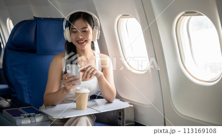 An attractive woman is using her phone and listening to music on her headphones during the flight. An attractive woman is using her phone and listening to music on her headphones during the flight. 113169108