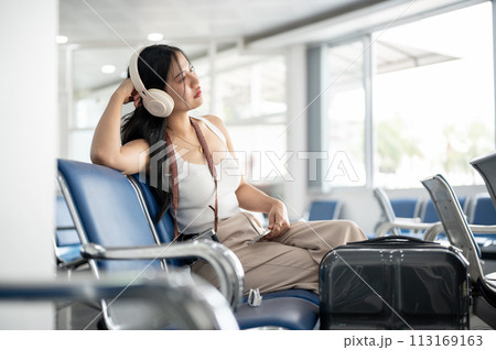 A female passenger is waiting for her boarding call in the airport terminal, looking at the runway. A female passenger is waiting for her boarding call in the airport terminal, looking at the runway. 113169163