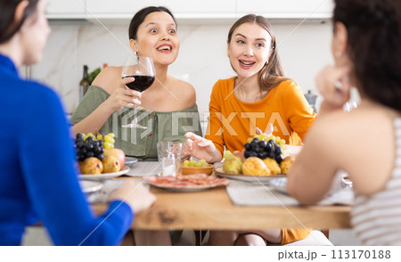 Girlfriends drinking wine and having conversation over dinner at house party Girlfriends drinking wine and having conversation over dinner at house party 113170188