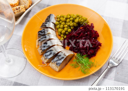 Slices herring fish with canned green peas, beetroot, decorated by mint served on plate with bread and cutlery Slices herring fish with canned green peas, beetroot, decorated by mint served on plate with bread and cutlery 113170191