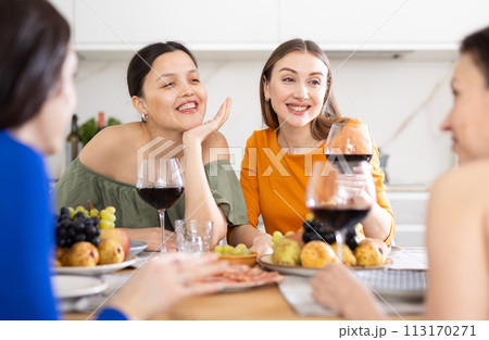 Four women are sitting at table, enjoying food and wine, chatting, talking, laughing. 113170271