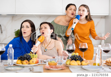 Cheerful female friends singing together at home karaoke Cheerful female friends singing together at home karaoke 113170358