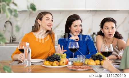 Girlfriends chatting and drinking wine in kitchen 113170440