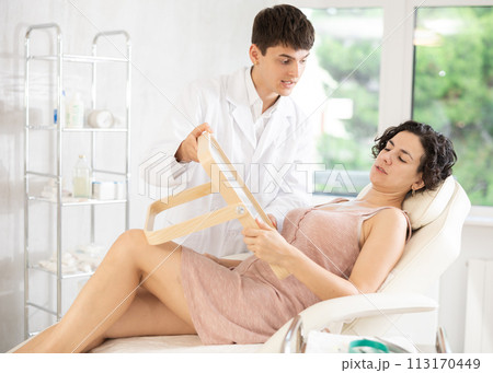 Male beautician giving consultation to woman patient with mirror in aesthetic clinic Male beautician giving consultation to woman patient with mirror in aesthetic clinic 113170449