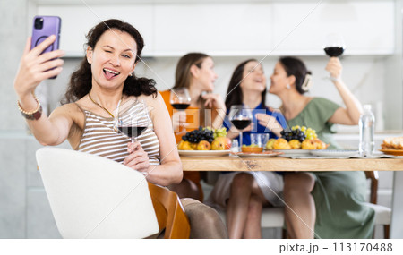Caucasian smiling girl is sitting on chair and taking selfies during gatherings with friends 113170488