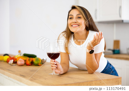 Portrait of woman with glass of red wine in modern kitchen - housewife prepares a vegetable salad and drinks red wine Portrait of woman with glass of red wine in modern kitchen - housewife prepares a vegetable salad and drinks red wine 113170491