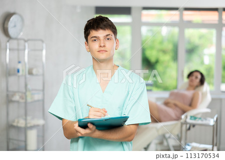 Young man doctor posing in doctor's cabinet with document in hands Young man doctor posing in doctor's cabinet with document in hands 113170534