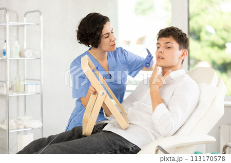 Beautician woman using mirror consulting man in clinic 113170578