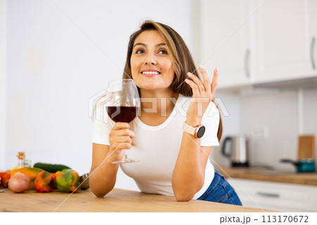 Happy housewife preparing vegetable salad and drinking red wine 113170672