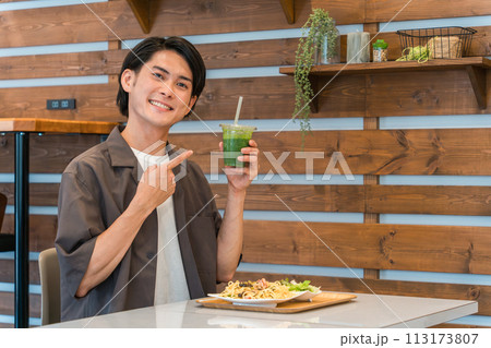 カフェでランチを食べながらグリーンスムージーを飲む若い男性（酵素・デトックス・食物繊維・健康食品） 113173807