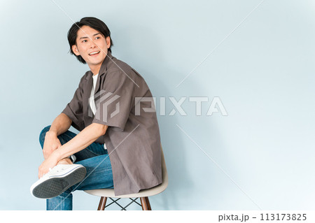 椅子に座るスニーカーとジーンズ姿のさわやかな男性 椅子に座るスニーカーとジーンズ姿のさわやかな男性 113173825