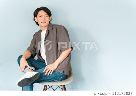椅子に座るスニーカーとジーンズ姿のさわやかな男性 椅子に座るスニーカーとジーンズ姿のさわやかな男性 113173827