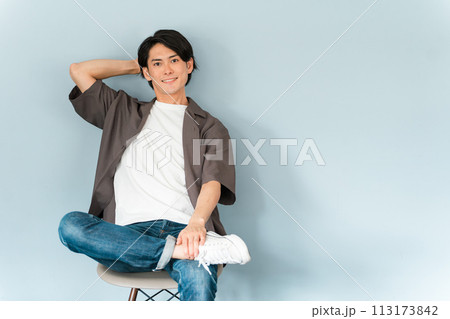 椅子に座るスニーカーとジーンズ姿のさわやかな男性 椅子に座るスニーカーとジーンズ姿のさわやかな男性 113173842