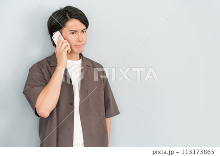 スマホで通話・電話する若いアジア人男性（怪しむ・不審・アポ電・詐欺・不審電話・迷惑電話） 113173865