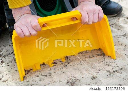 A boy in a yellow jacket is a toy car in the sand 113178506
